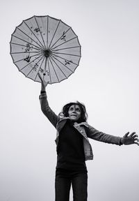 Low angle view of woman jumping for umbrella against clear sky