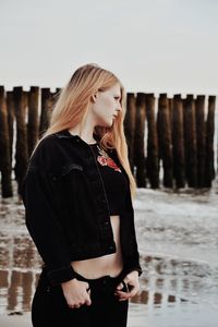 Young woman standing at beach against sky