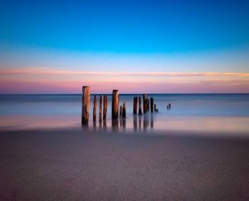 Wooden posts on beach against sky during sunset