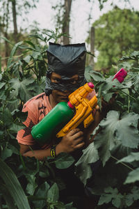 Portrait of boy holding water gun amidst plants