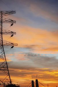 Low angle view of silhouette electricity pylon against dramatic sky during sunset