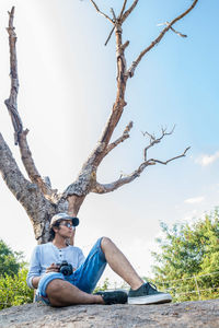 Young woman sitting on tree trunk against sky in park