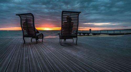 Rear view of man and woman sitting on deck chairs at beach