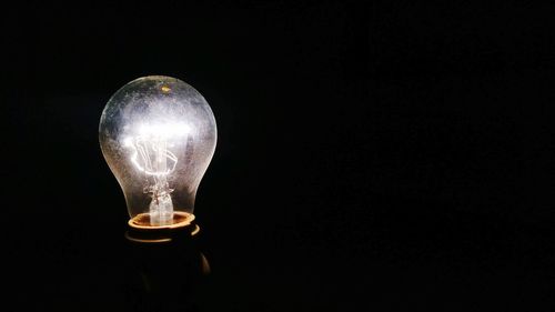 Close-up of illuminated light bulb against black background