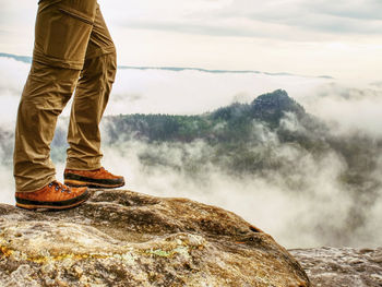 Man hiker legs with windproof trousers and hiking boots on mountain peak with a valley at background