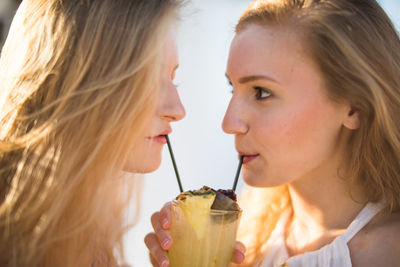 Close-up of female friends drinking drink while standing face to face