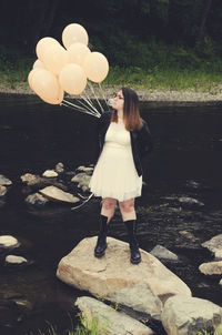 Woman blowing bubble gum while standing on rock at lake