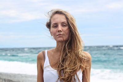 Portrait of young woman standing at beach against sky