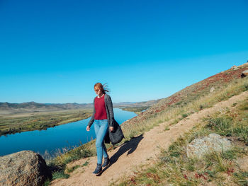 Full length of woman walking on mountain against clear blue sky
