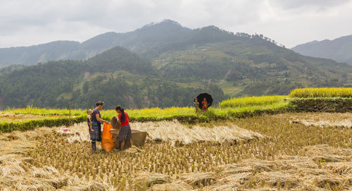 Men sitting on field by mountains against sky