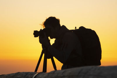 Silhouette woman photographing against sky during sunset