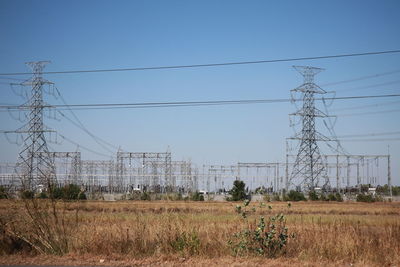 Electricity pylons on field against clear sky