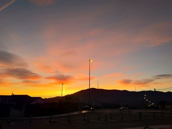 Street by silhouette city against orange sky