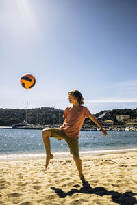 Full length of boy playing with ball on beach against sky during sunny day