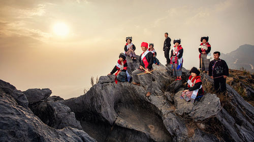 People on rock against sky during sunset