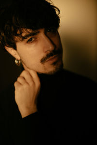 Young man with mustache next to wall looking at camera