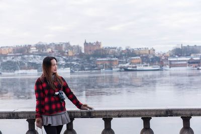 Woman standing by railing against river in city