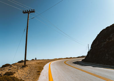 Road by electricity pylon against sky