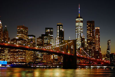 Illuminated buildings by river against sky in city at night