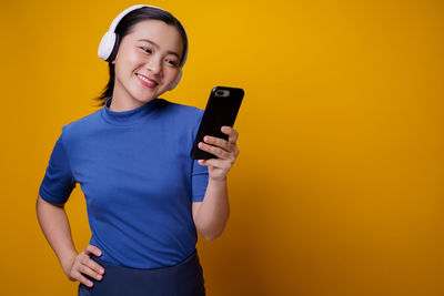 Full length of a smiling young man using smart phone against yellow background