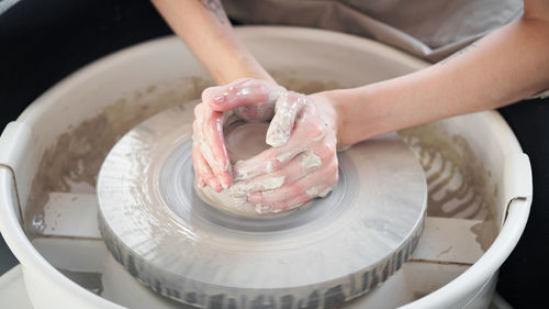 Midsection of woman making pot on pottery wheel