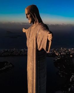 Statue looking at sea by city against sky at night