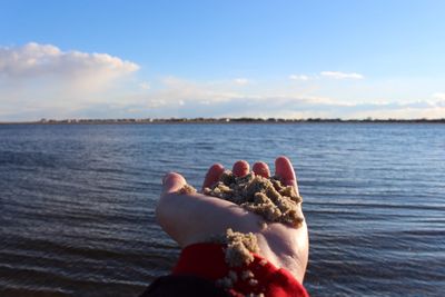 Woman's hand on beach against sky