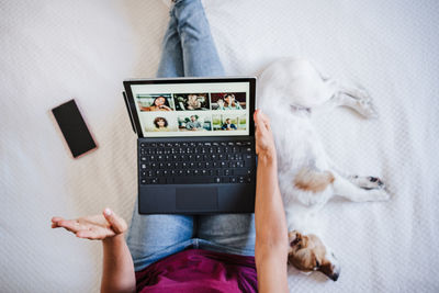 Woman at home doing video call with friends on mobile phone while jack russell dog resting on bed