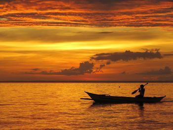 Silhouette man in sea against dramatic sky during sunset