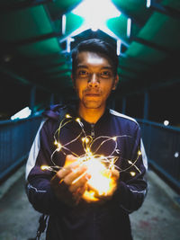 Portrait of smiling man holding illuminated string lights while standing on elevated walkway