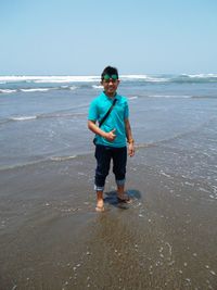 Portrait of young man showing thumbs up while standing at beach against clear sky