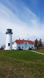 Lighthouse on field by building against sky