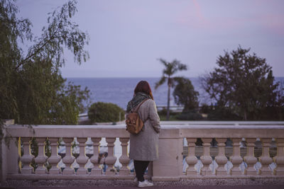 Rear view of woman standing by railing against sky