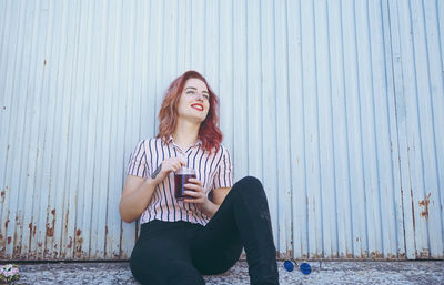 Portrait of young woman sitting against wall