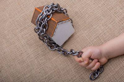Cropped hand of child holding chain tied to model home on burlap