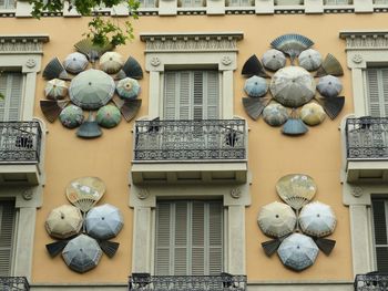 Sculpture of umbrellas and fans on wall between two shuttered balconies