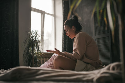 Midsection of man using mobile phone while sitting on bed at home