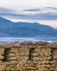 Stone wall by mountains against sky