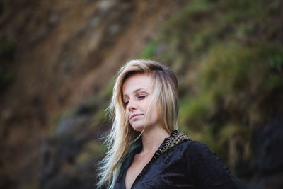 Close-up of young woman standing against rocky mountain