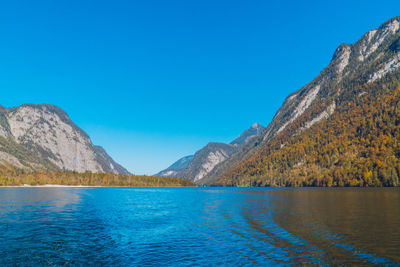 Scenic view of lake by mountains against clear blue sky