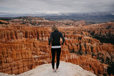 Rear view of woman standing on rock against sky