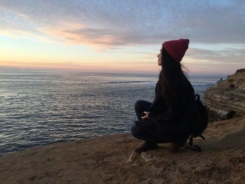 Young woman on rock formation by sea against sky during sunset