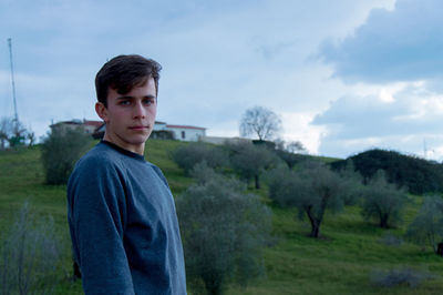 Portrait of young man standing on field against sky