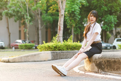 Portrait of smiling woman sitting on plant against trees