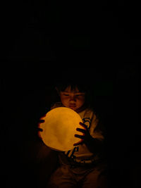 Low angle view of a child holding a moon lamp against black background