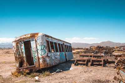 Old abandoned train on field against blue sky during sunny day