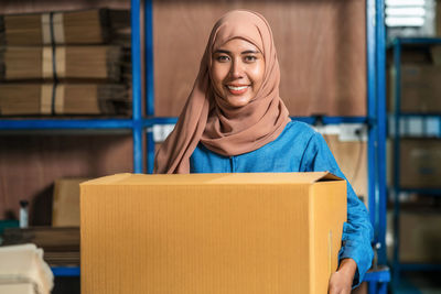 Portrait of smiling young woman holding cardboard box