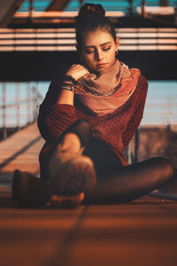 Young woman looking away while sitting on floor