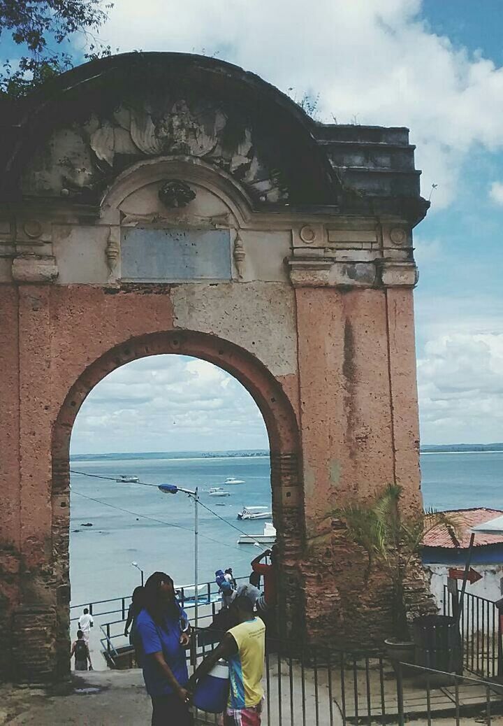 architecture, built structure, building exterior, sky, sea, water, lifestyles, cloud - sky, men, beach, leisure activity, person, horizon over water, arch, cloud, day, outdoors, incidental people