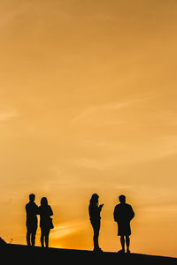 Silhouette people standing against orange sky